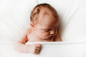 Newborn photography, baby lays sleeping tucked into white sheets